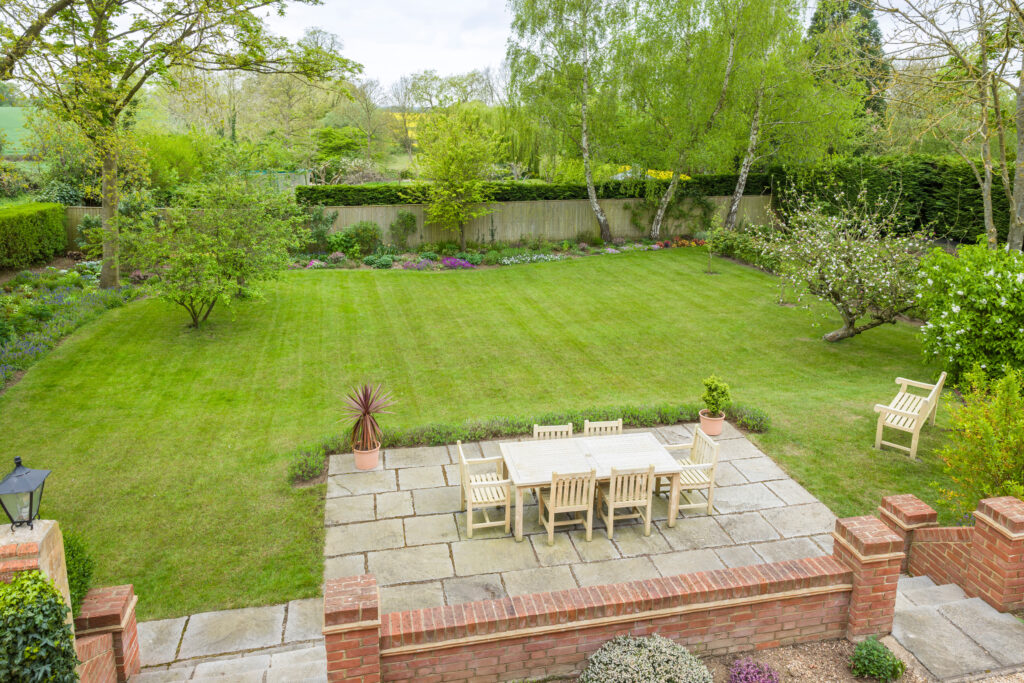 Wooden garden furniture on a patio terrace in a UK landscaped back garden with large lawn